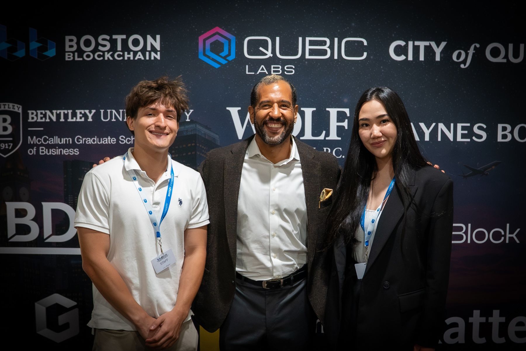 Ian Cain with two members of the Boston Blockchain Week team in front of the QUBIC Labs backdrop
